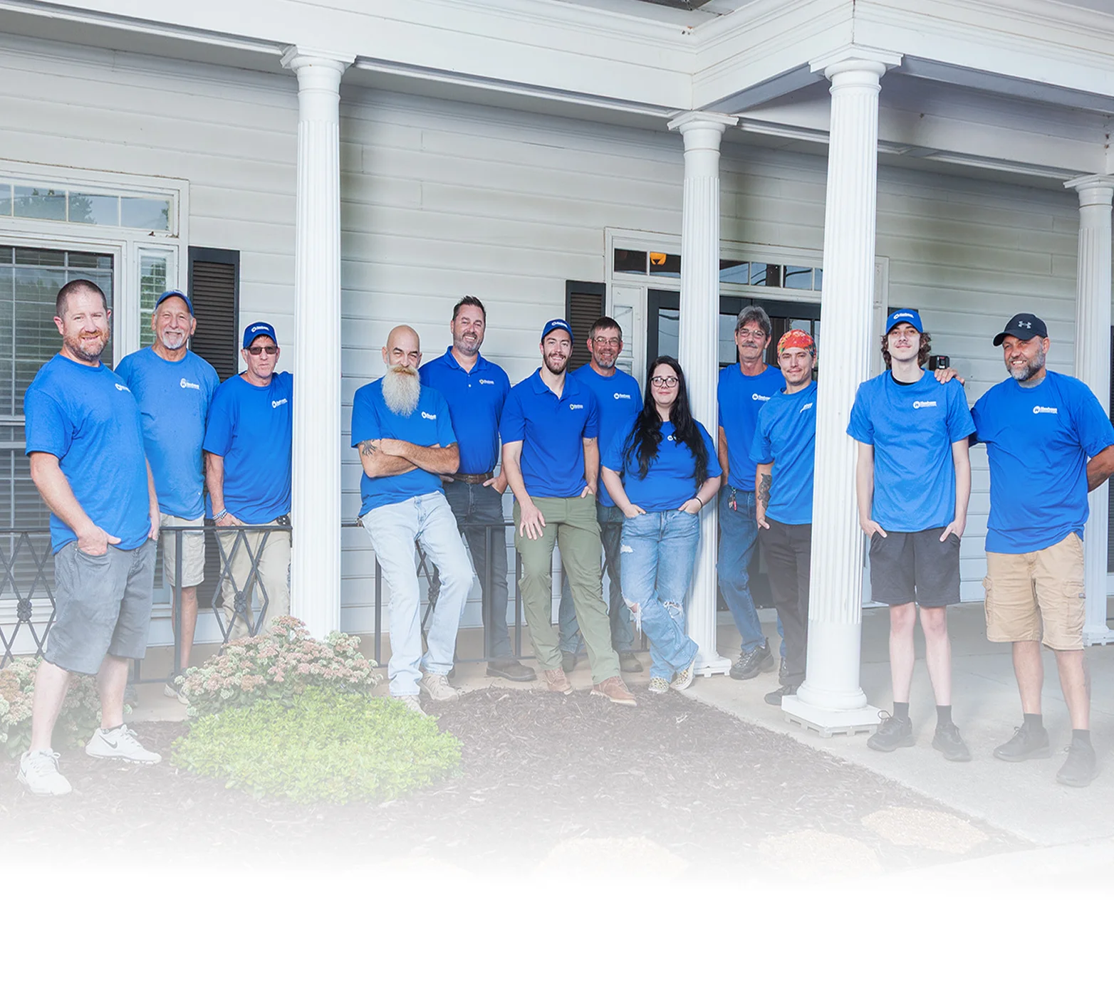 Team of gutter installation professionals standing together outside a home, wearing matching blue company shirts on a front porch with white columns.