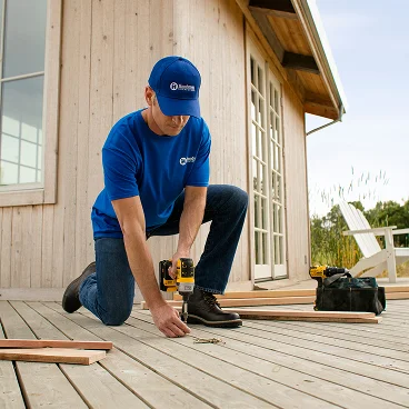 Professional installing wooden deck boards using a power drill during deck construction.