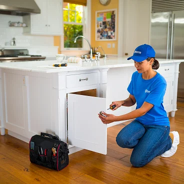 Home service professional kneeling on a kitchen floor repairing or adjusting a cabinet door.