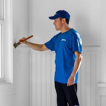Painter carefully painting interior trim and wall detail with a brush.